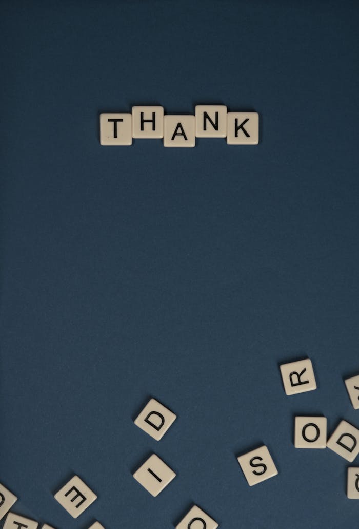 Scrabble tiles spelling 'Thank' set against a blue backdrop, ideal for messages of gratitude.